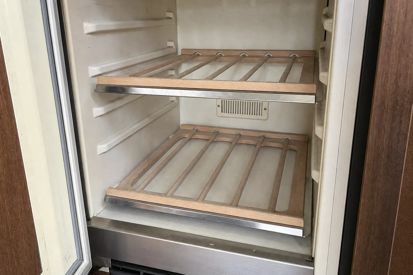 Empty undercounter wine cooler interior with two wooden slide-out racks and the glass door open